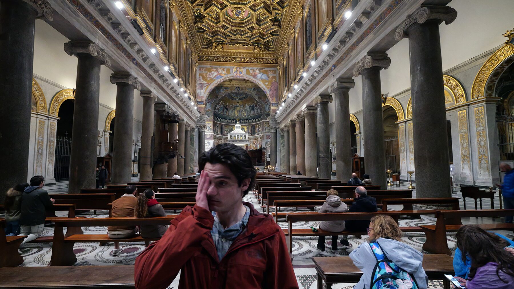 A man shields one eye from the light inside a gilded Roman basilica